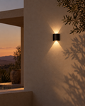 Piana compact black IP65 outdoor wall light beside a stone step, grazing a low band of warm light across the wall
