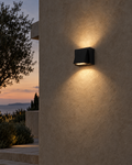 Cala matte black up and down wall light mounted on a rendered exterior wall at dusk, casting two wedges of warm light