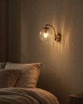 Riva clear blown-glass wall sconce on a black arm against a plastered wall beside a mirror