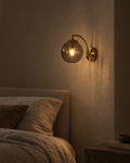 Riva smoke grey glass wall sconce in a dark hallway, the shade lit and the bulb hidden