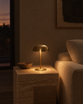 Nuvo brushed brass cordless table lamp on a console beside a book, warm light on the wall behind