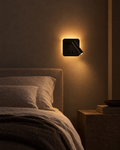 Lume square matte black reading sconce on a panelled wall with its reading spot angled down